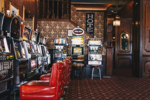 A vintage-style casino interior featuring rows of slot machines and plush red seating.