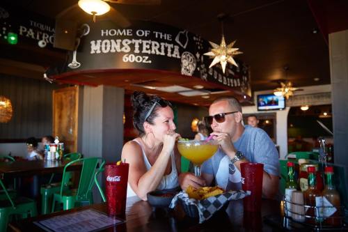 A couple shares a large drink at a vibrant restaurant, enjoying nachos and each other's company.