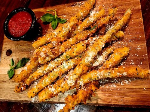 Crispy breadsticks topped with cheese, served on a wooden board with a side of marinara sauce.