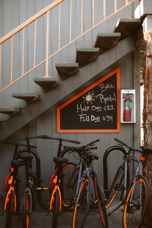 Bicycles parked near a staircase with a chalkboard sign for bike rental prices.