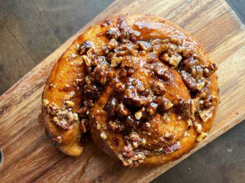 A close-up of a sticky cinnamon roll topped with chopped nuts on a wooden board.