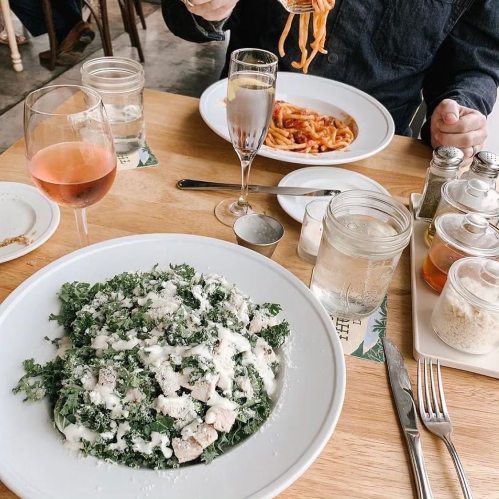 A table set with a salad, pasta, and drinks, with a person holding a fork above a plate of spaghetti.