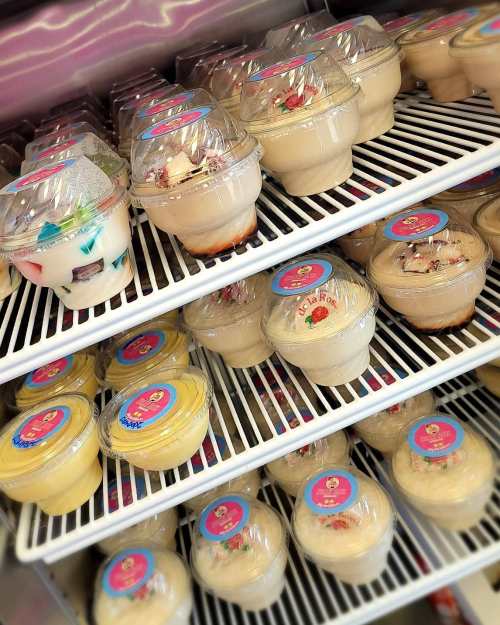 A display of various dessert cups with colorful lids, arranged neatly on shelves in a refrigerator.