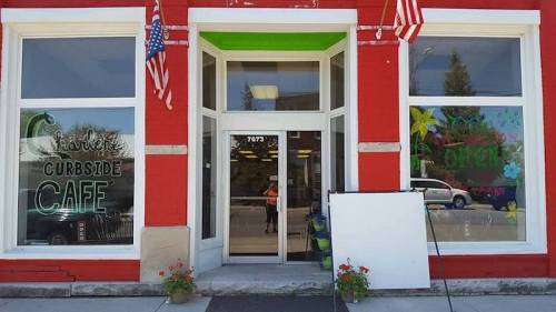 Front view of a red café with large windows, featuring "Curbside Café" signage and American flags.