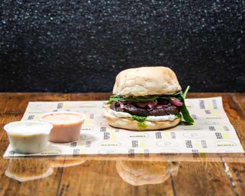 A delicious burger with greens, served on a wooden table alongside two dipping sauces.