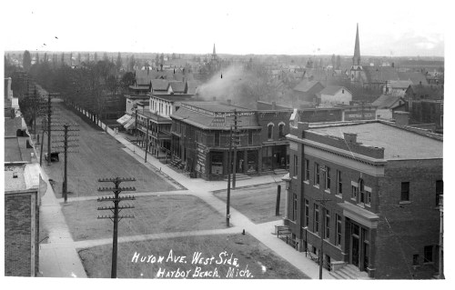 Black and white photo of Huron Ave, West Side, Harbor Beach, Michigan, showing buildings and a distant church steeple.