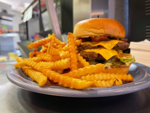 A plate with a cheeseburger topped with bacon and lettuce, accompanied by a serving of crinkle-cut fries.