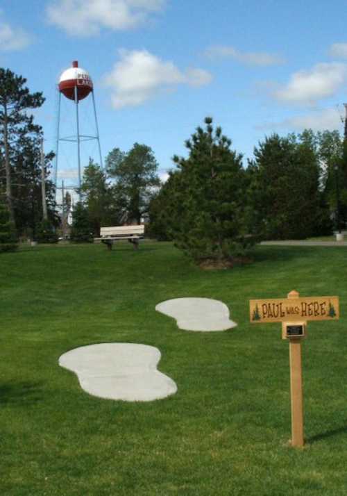 A park scene featuring a water tower, trees, and a sign that reads "PAUL WAS HERE" near a grassy area.