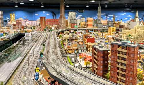 A detailed miniature cityscape with train tracks, buildings, and vehicles, showcasing vibrant urban life.