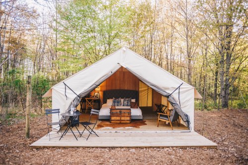 A cozy glamping tent with a bed and seating area, set in a wooded outdoor environment.