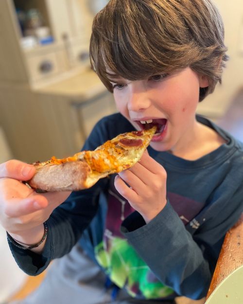 A young boy with brown hair enjoys a slice of pizza, preparing to take a big bite.