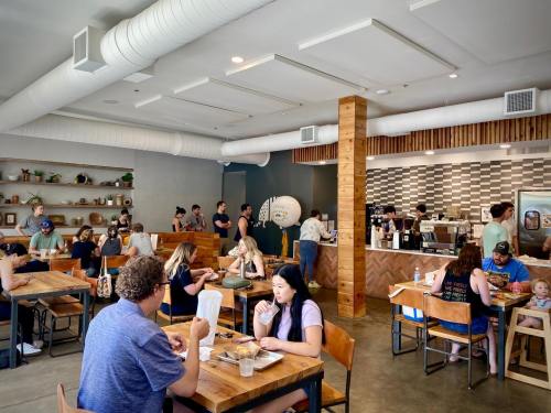 A busy café interior with patrons dining and ordering at the counter, featuring wooden tables and a modern design.