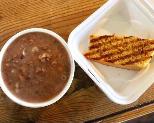 A bowl of hearty soup with chunks of meat, accompanied by a slice of toasted bread on a wooden table.