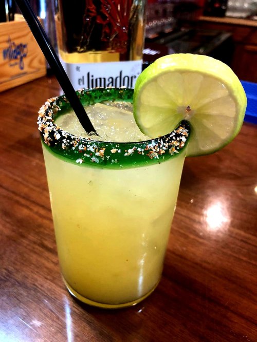 A refreshing cocktail with a green rim, garnished with a lime slice and served with a straw on a wooden bar.