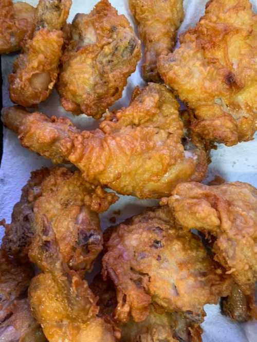 A close-up of crispy, golden-brown fried chicken pieces on a white paper towel.