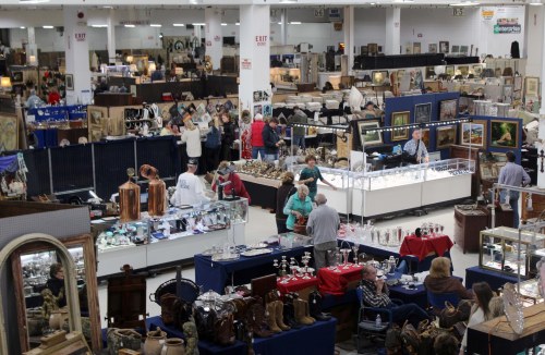 A bustling antique market with various vendors, displays of items, and shoppers exploring the booths.