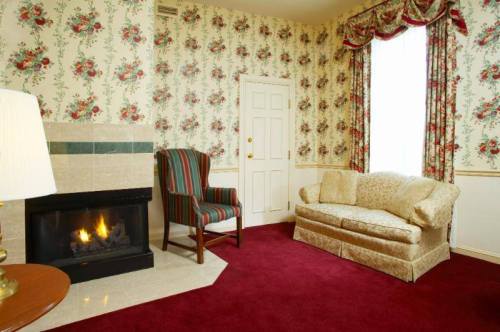 Cozy room with floral wallpaper, a fireplace, a striped armchair, and a plush sofa on a red carpet.