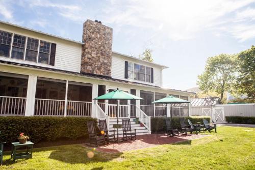 A charming house with a stone chimney, surrounded by green grass and patio seating under umbrellas on a sunny day.