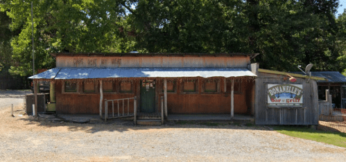 A rustic bar and grill building with a metal roof, surrounded by trees and gravel, featuring a sign for "Donnelly's."