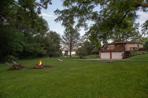 A serene backyard scene featuring a fire pit, green lawn, and a house surrounded by trees at dusk.