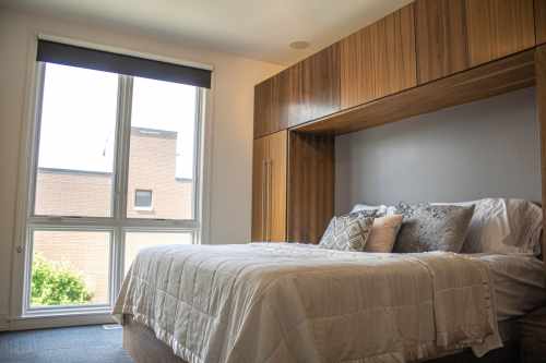 Cozy bedroom featuring a bed with a white quilt, decorative pillows, and large windows with natural light.