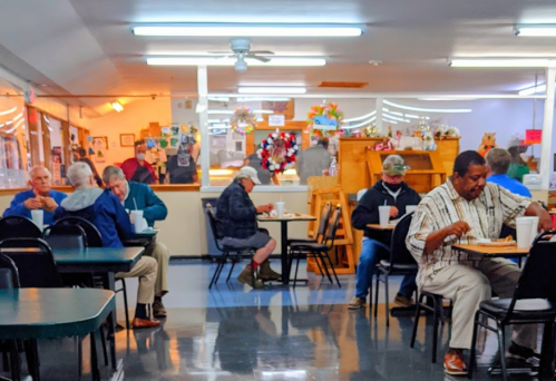 A busy diner scene with several patrons eating at tables, a counter in the background, and a casual atmosphere.