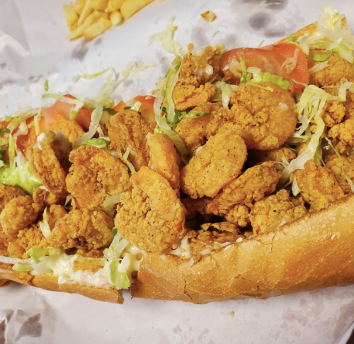 A loaded shrimp po' boy sandwich with lettuce, tomatoes, and mayonnaise on a toasted hoagie roll.