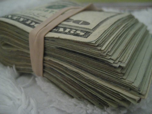 A stack of cash wrapped with a rubber band, resting on a textured surface.