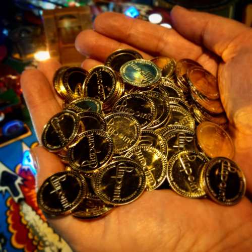 A hand holding a pile of shiny coins, some gold and some copper, against a colorful background.