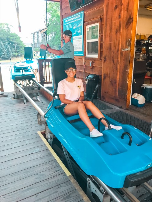 A person sits in a blue mountain coaster cart, smiling, with a wooden building in the background.