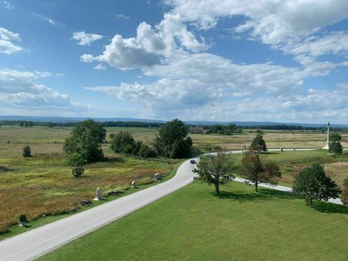 A scenic view of a winding road through a grassy landscape under a blue sky with fluffy clouds.