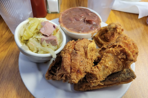 A plate of fried chicken with sides of coleslaw and beans on a wooden table.