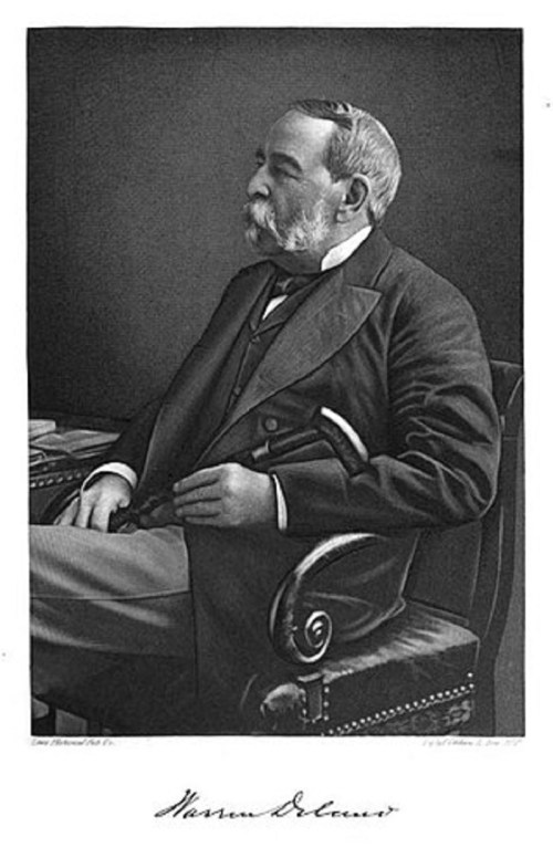 A black and white portrait of a distinguished man with a mustache, seated in a chair, wearing a formal suit.