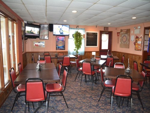A cozy restaurant interior with wooden walls, tables, red chairs, and multiple TVs on the wall.