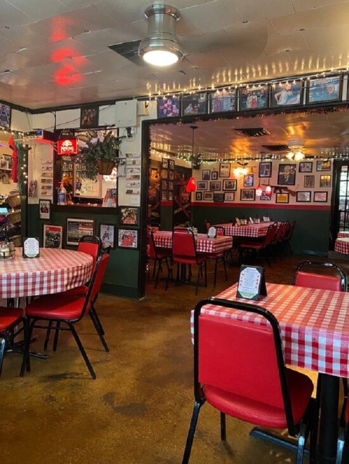 Cozy restaurant interior with red checkered tablecloths, red chairs, and walls adorned with framed photos.