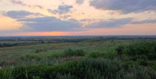 A serene landscape at sunset, featuring rolling hills, green grass, and a colorful sky with scattered clouds.