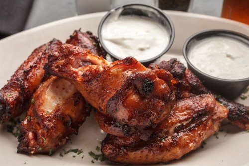 A plate of grilled chicken wings served with two dipping sauces, garnished with herbs.