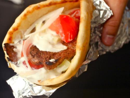 A hand holding a wrapped pita filled with grilled meat, tomatoes, onions, and sauce.