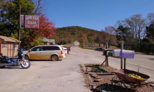 A scenic view of Low Gap Café along a rural road, with autumn foliage and parked vehicles in the background.