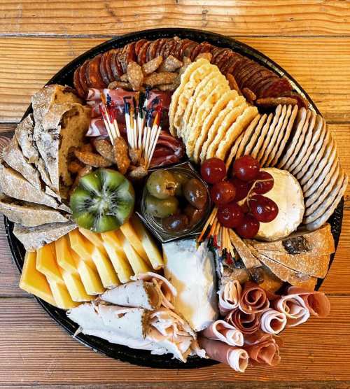 A colorful charcuterie board featuring meats, cheeses, fruits, nuts, and crackers arranged on a wooden table.