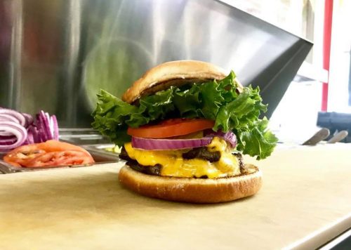 A delicious cheeseburger with lettuce, tomato, onion, and a toasted bun, set on a countertop in a kitchen.