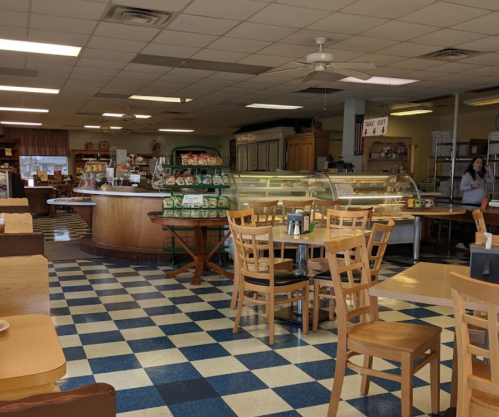 Cozy café interior with wooden tables, a display case, and a checkered floor, featuring a barista in the background.