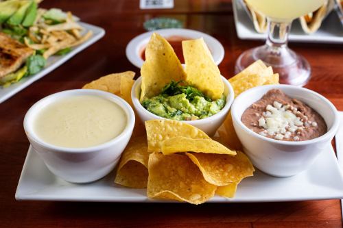 A plate of tortilla chips with guacamole, cheese dip, and refried beans in small bowls.