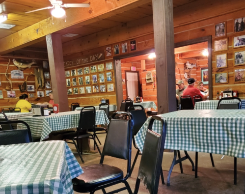 Interior of a rustic restaurant with wooden walls, checkered tablecloths, and framed photos on the walls.