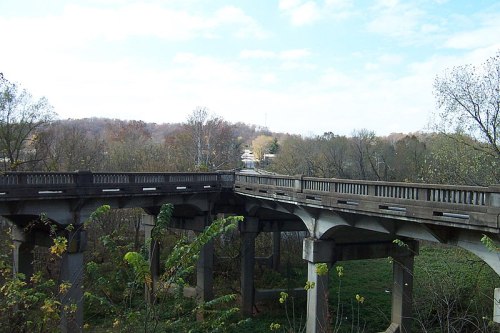 An abandoned concrete bridge surrounded by trees and greenery under a clear blue sky.