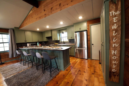 Modern kitchen with green cabinets, stainless steel appliances, and a wooden sign reading "The Edlin House." Cozy atmosphere.