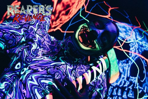 A person in a colorful, psychedelic outfit poses under blacklight, with vibrant patterns and a playful expression.