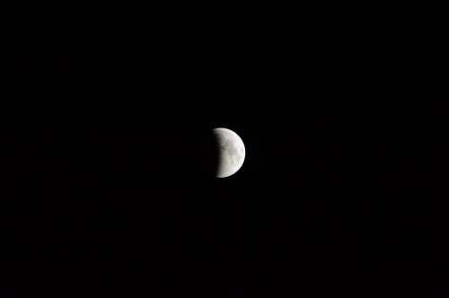 A partially illuminated moon against a dark night sky, showcasing its craters and surface details.