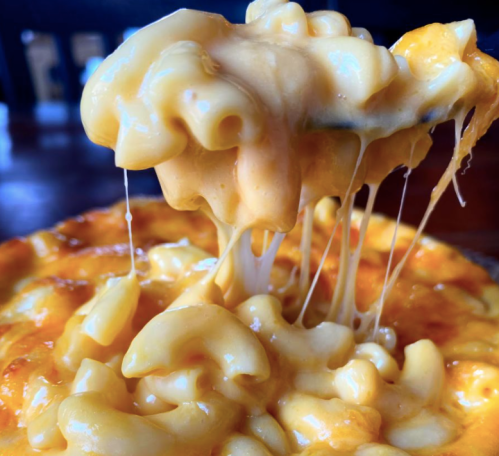 A close-up of creamy, cheesy macaroni and cheese with gooey cheese stretching from a spoon.