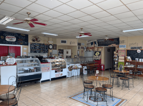 A cozy café interior with tables, a display case, and chalkboard menus on the walls. Ceiling fans add a welcoming touch.